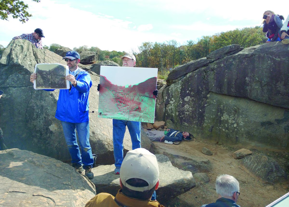 Center for Civil War Photography Vice President Garry Adelman (left) and Imaging Director John Richter, hold up the 2-D and 3-D versions of the famous ‘dead sharpshooter’ photo at Devil’s Den while reenactor Bryan Parkhurst plays the role of the dead Confederate at the 16th annual Image of War seminar.