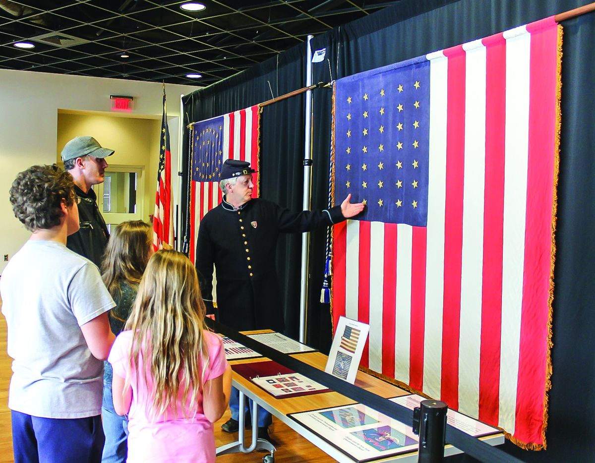 CWDF Flag Display. Tyrone Cornbower points out different designs of the National Color during the CWDF’s “The Colors of the Blue,” a display of Union Army flags at the GNMP Visitor Center. (CWDF Photo)