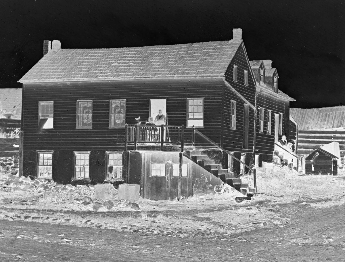 This Brady image, taken from half of a stereo negative, shows citizen hero John Burns sitting on the porch of his house. At right, sitting on the steps is the straw-hatted Brady. To his right, mounted on a tripod behind the water well, is Brady’s portable darkroom.
