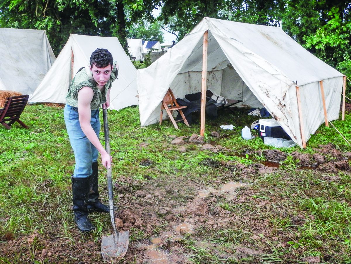 Ethan Miller, from Scottsville, Ky., works to divert rain water from his tent.