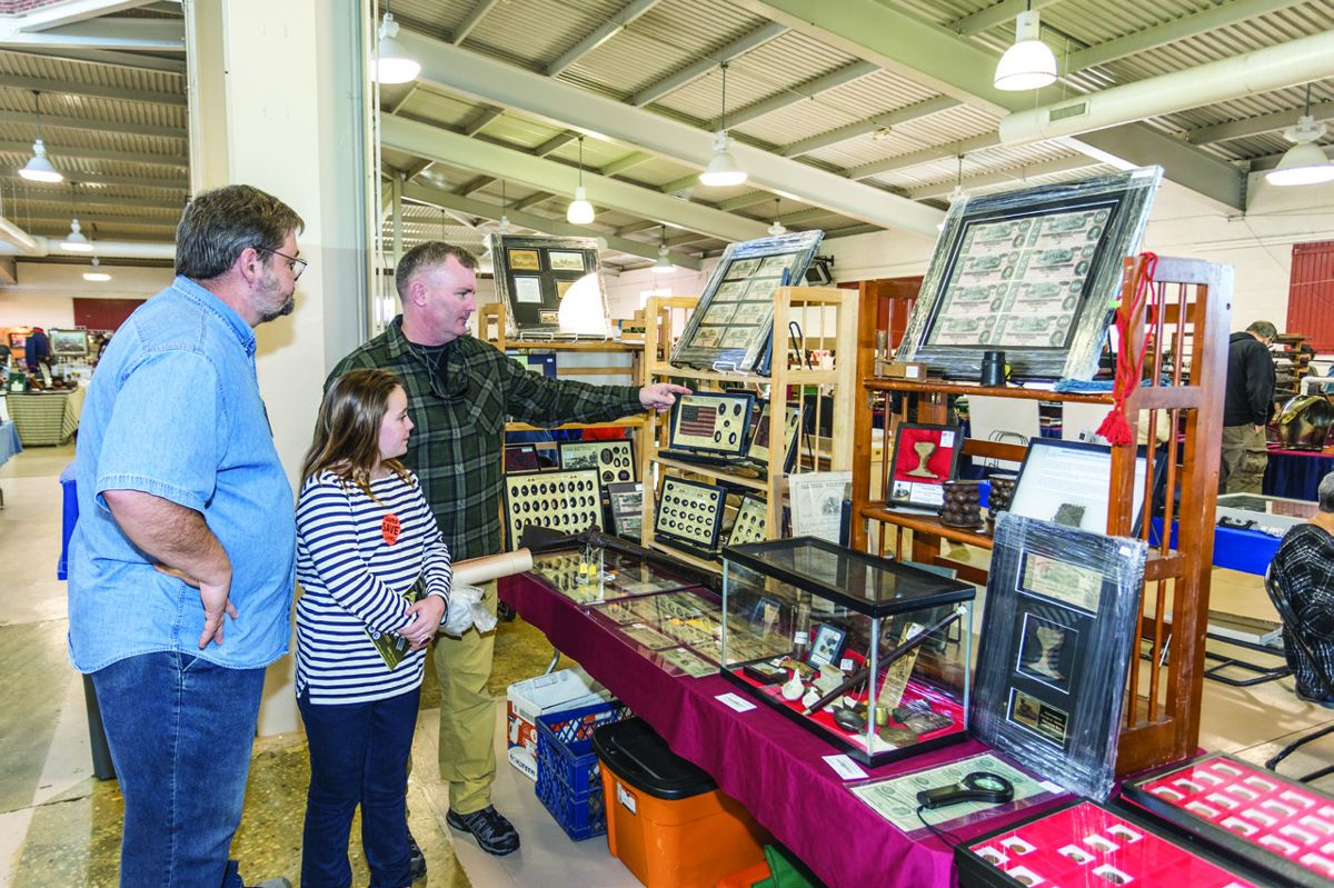 Harvey Warrner, owner of Iron Brigade Relics, helping customer Jim Murphy and daughter Harper Murphy decide on what to buy.