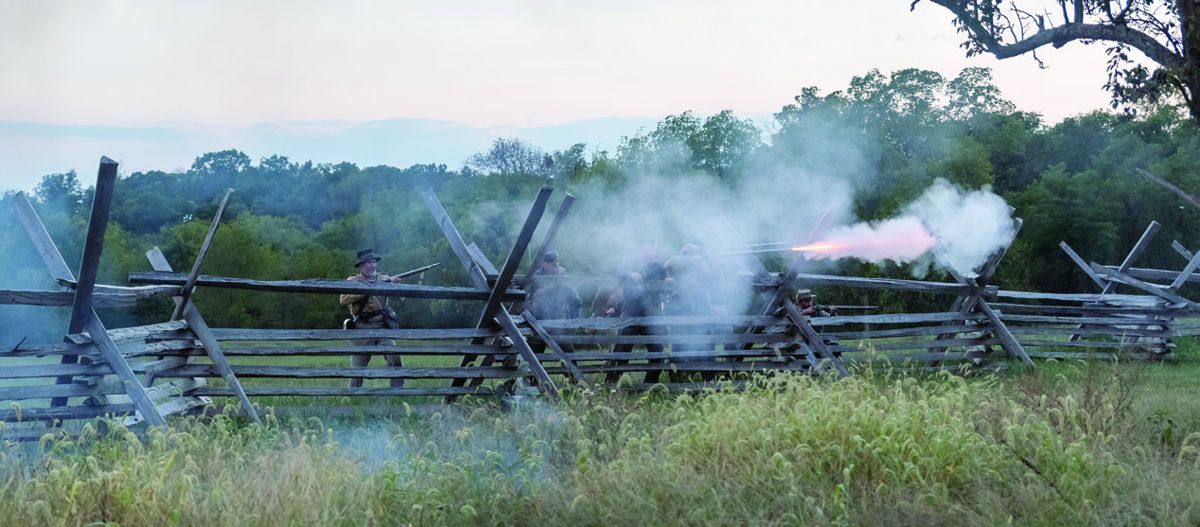 Confederates reenactors firing from behind a rail fence.