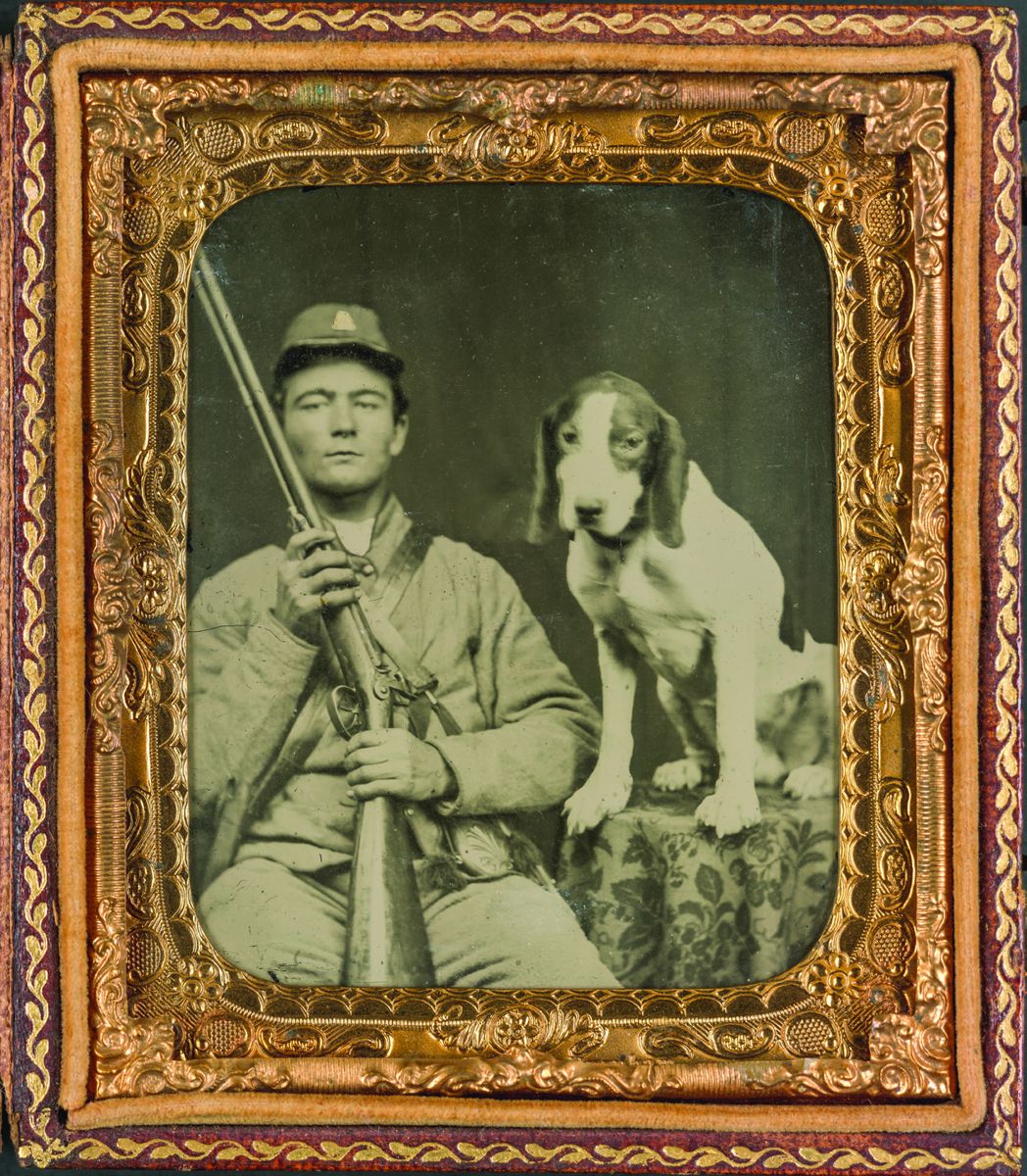 Unidentified soldier in Confederate uniform holding a double- barrel shotgun while sitting next to a dog. (Liljenquist Family Collection of Civil War Photographs. Library