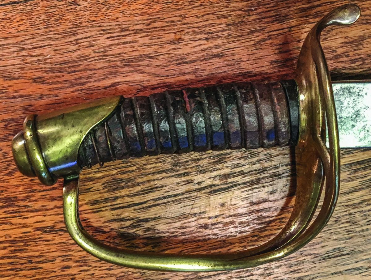 The carved wood grip of this sword was originally completely covered with leather, which is worn; and only 3 strands of the original, single brass wire wrap are retained.