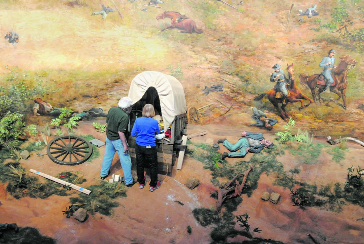 One of the more famous illusions in The Battle of Atlanta is a damaged wagon with its front wheels in the painting and its back wheels in the diorama. Here, engineer Tom Diehl and scenic artists install a new wagon to replace the old one damaged by dry-rot.