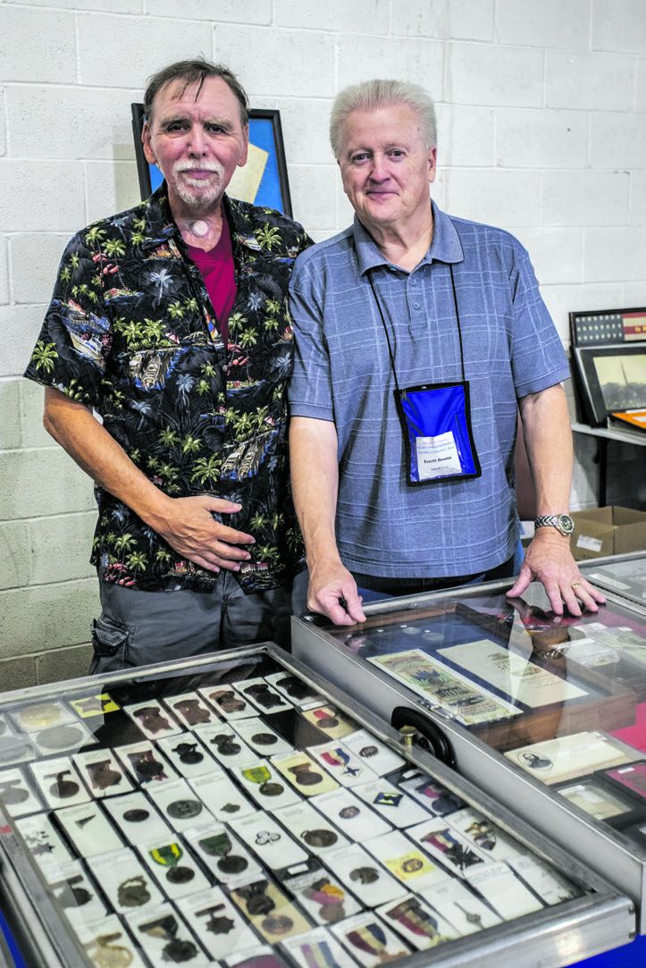 Dan Toomey and Everitt Bowles pose for a photo in front of Everitt’s assorted UCV, SCV, UDC, and other reunion badges for sale from CivilWarBadges.com.