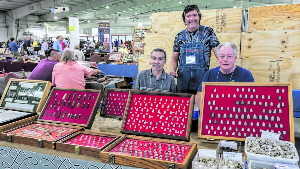 Les Wells, Nick Periut, and John Gibson smile for the camera behind Nick’s Army of Tennessee Relics tables of bullets, buttons, belt buckles, artillery, swords and rifles.
