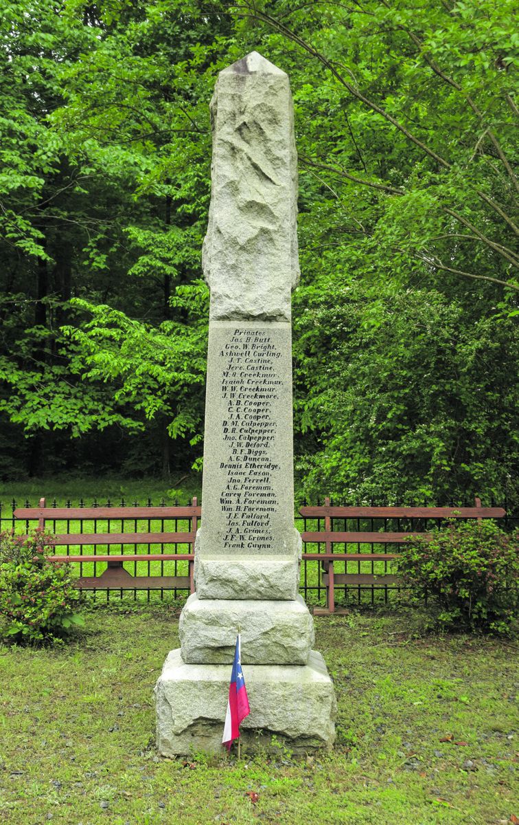This overview of the Jackson Greys monument site illustrates the monument, flagpole, benches, and fenced enclosure. The Jackson Greys monument site was developed with funds raised by the Norfolk County Grays Chapter of the United Daughters of the Confederacy. The Norfolk County Grays Chapter of the Sons of Confederate Veterans maintains the site.