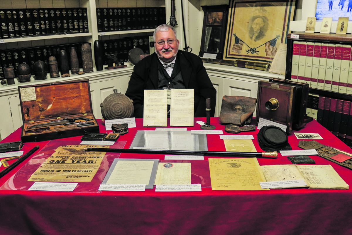 Mike Shovlin smiles for the camera behind a display of some of the rare artifacts in the ACHS collection.