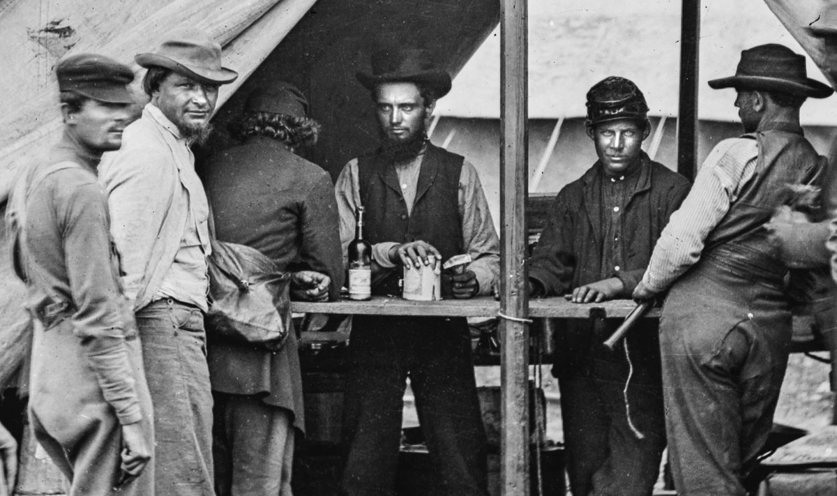 Enlargement of the photograph below. Note the bottle of alcohol to the left of the man in the center. Unfortunately the label is not clear enough to read.