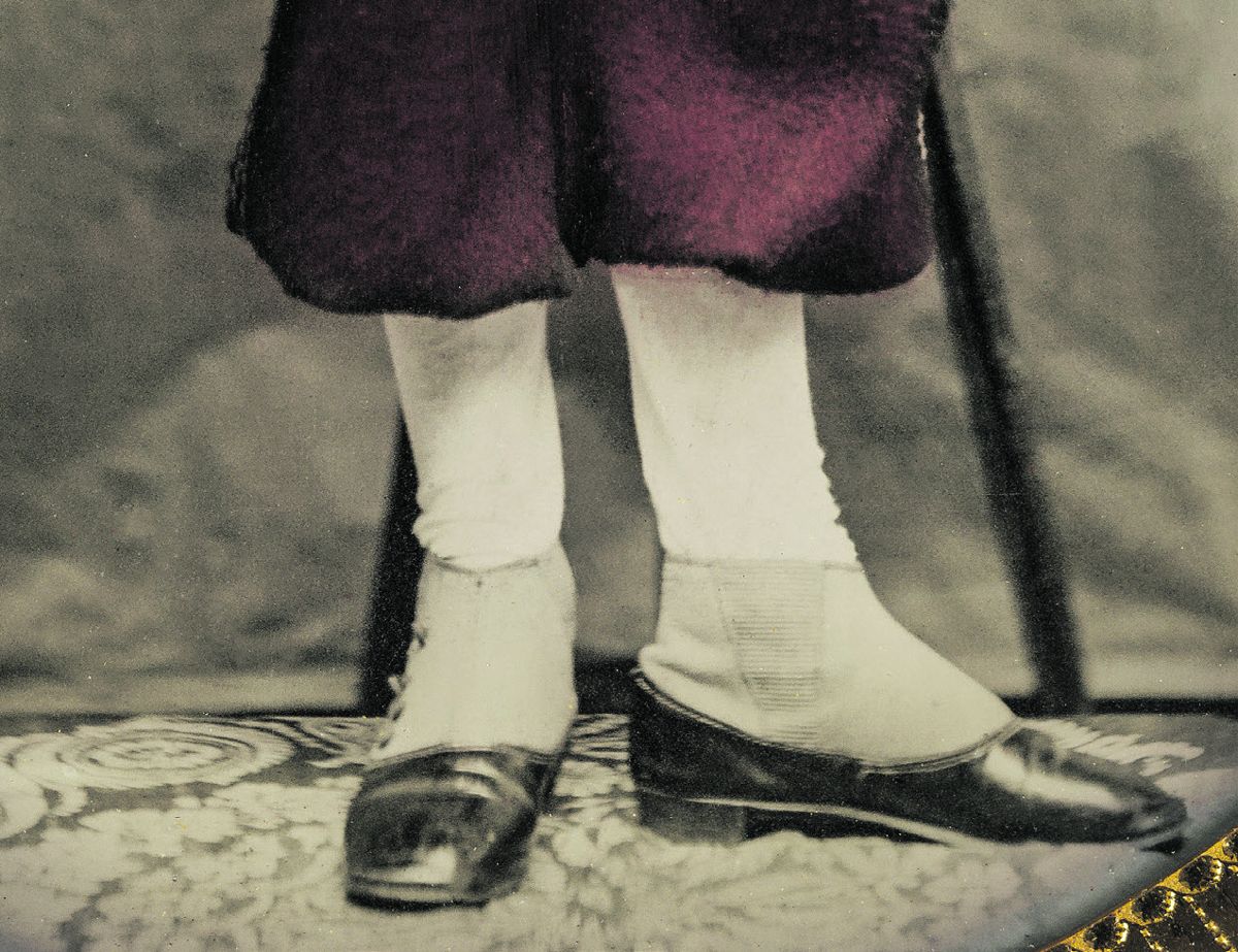 The red pantaloons are held up by buttoned flaps on both the outside and inside seam lines to create the expanded look. The lower spatter-dashes have a heavier, darker color to better wear and show less staining. The spats are outlined by the low cut of the shoes. They are highly polished or patent leather with a somewhat round toe.