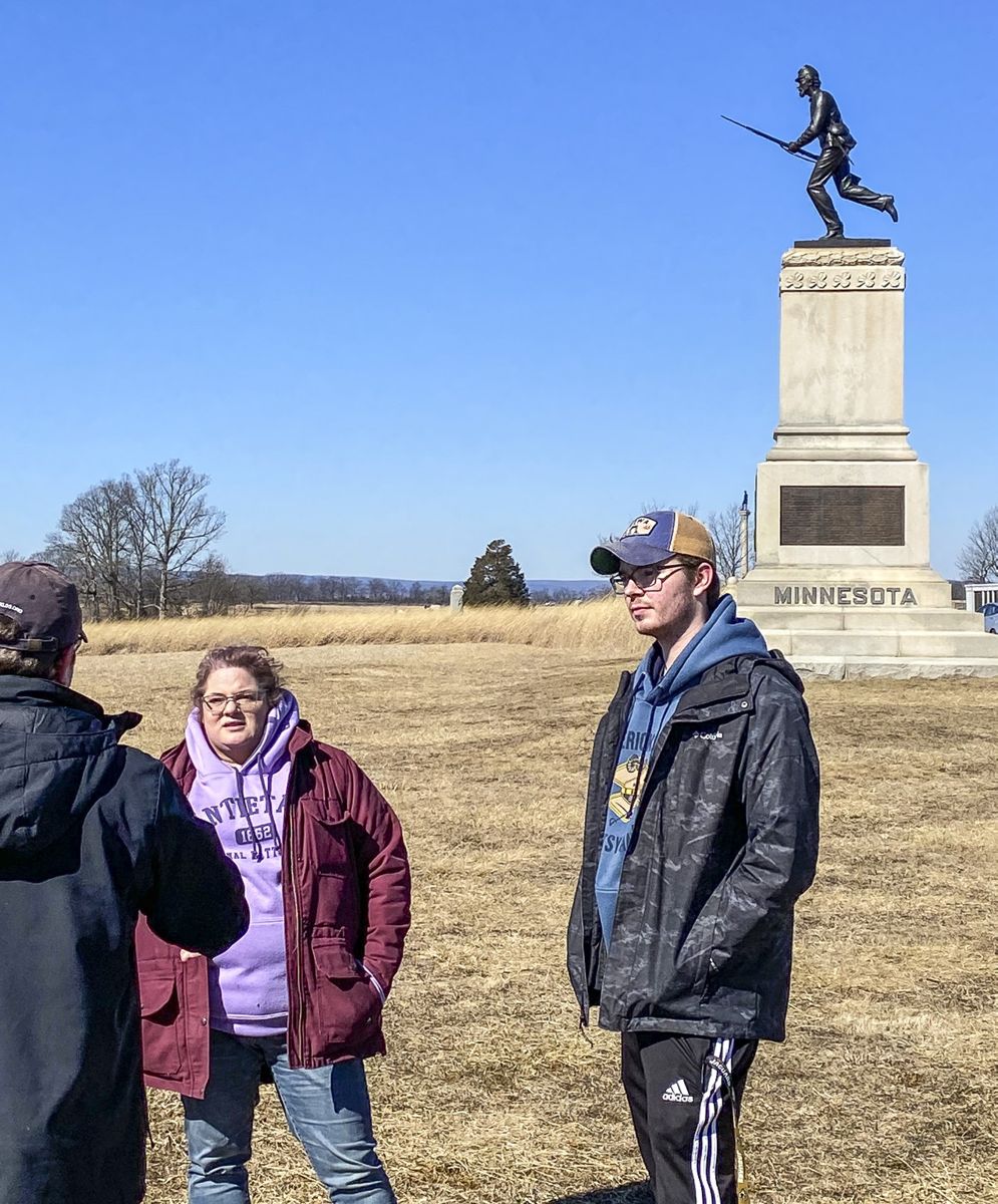 Caroline Davis and guest author Carson Ford talk with Kris White in the shadow of the First Minnesotans.