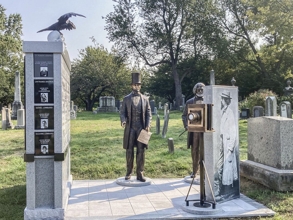 Overview of the Mathew Brady Memorial showing the photo gallery wall, the statues of Lincoln and Frederick Douglass, and the life size photograph of Brady posed with his camera. Congressional Cemetery, Washington, D.C.